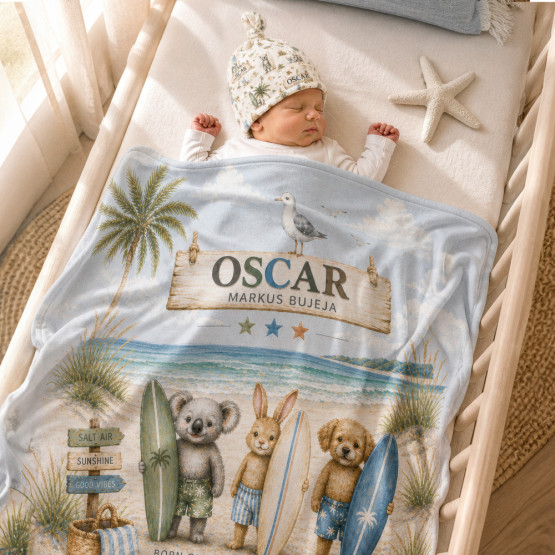 Personalised baby blanket and matching beanie set with coastal animal design, featuring a sleeping newborn wrapped in a soft blue beach-themed blanket with name Oscar printed, styled in a neutral nursery cot setting.